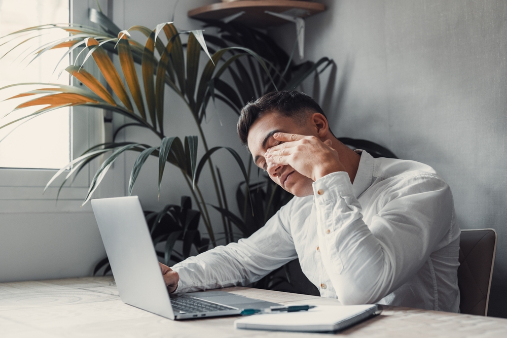 Young man with eye strain from spending too much time looking at a lap top